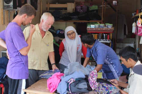With Tiwi's help, Tim and Jesse explain to the tailor that they want basketball jerseys made of the batik material they bought.